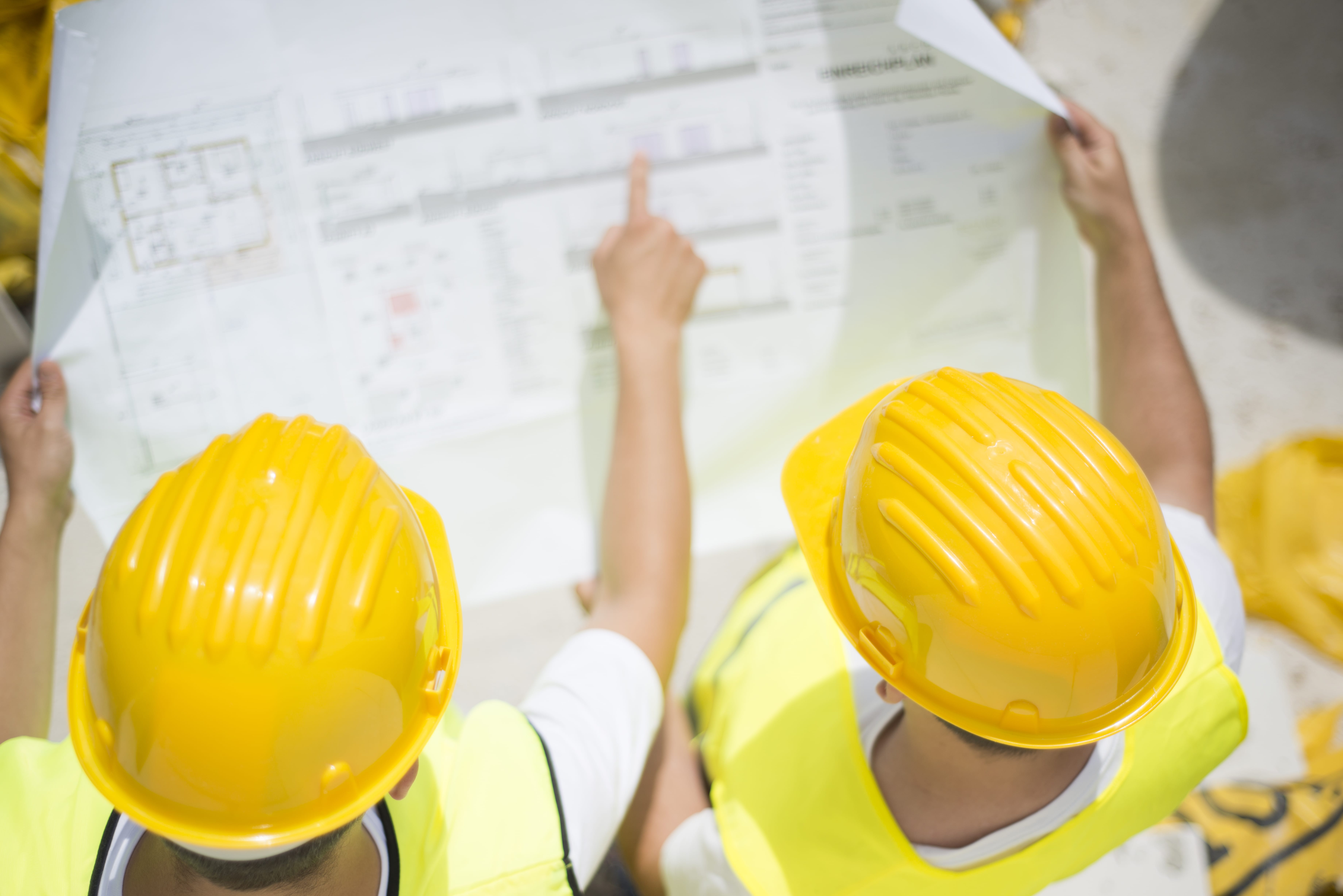 Engineer builders Construction workers in yellow safety vests and hard hats reviewing blueprints at a construction site, emphasizing teamwork and communication for project success.